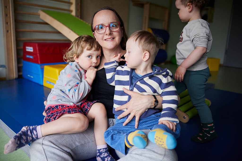 Eine Mitarbeiterin der Integrativen Kindereinrichtungen hat zwei Kinder auf ihrem Schoß.