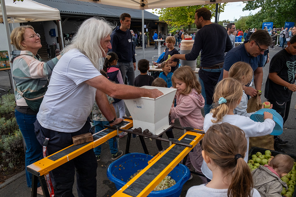 Beim Hof- und Kelterfest: Kinder und Mitarbeitende arbeiten Hand in Hand an der Kleltermaschine.