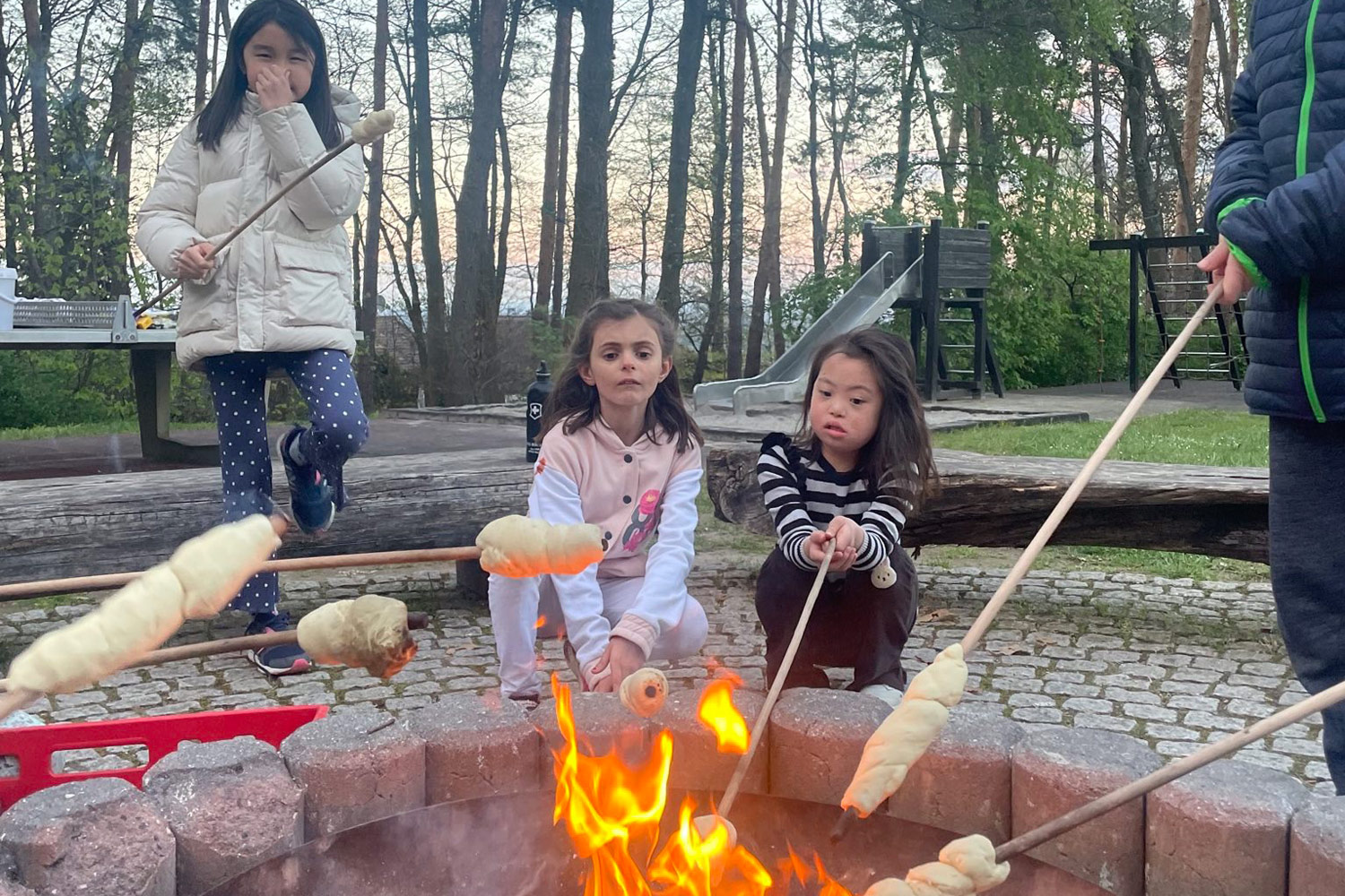 Die Kinder machen zusammen Stockbrot über einem Lagerfeuer.